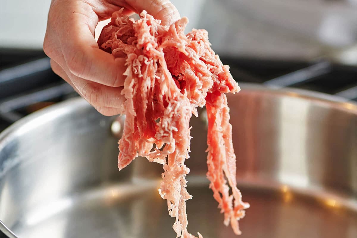 Woman placing raw shaved beef into pan on stove. 