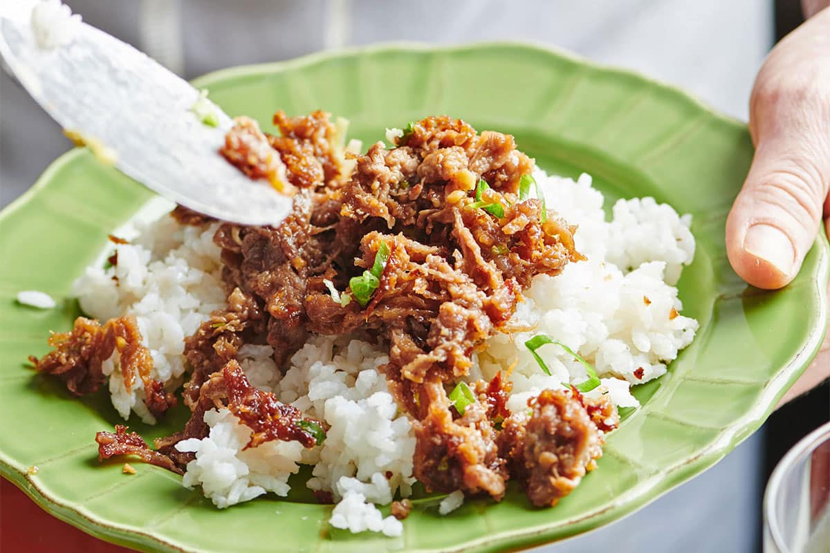 Serving Mongolian beef over white rice on green plate.