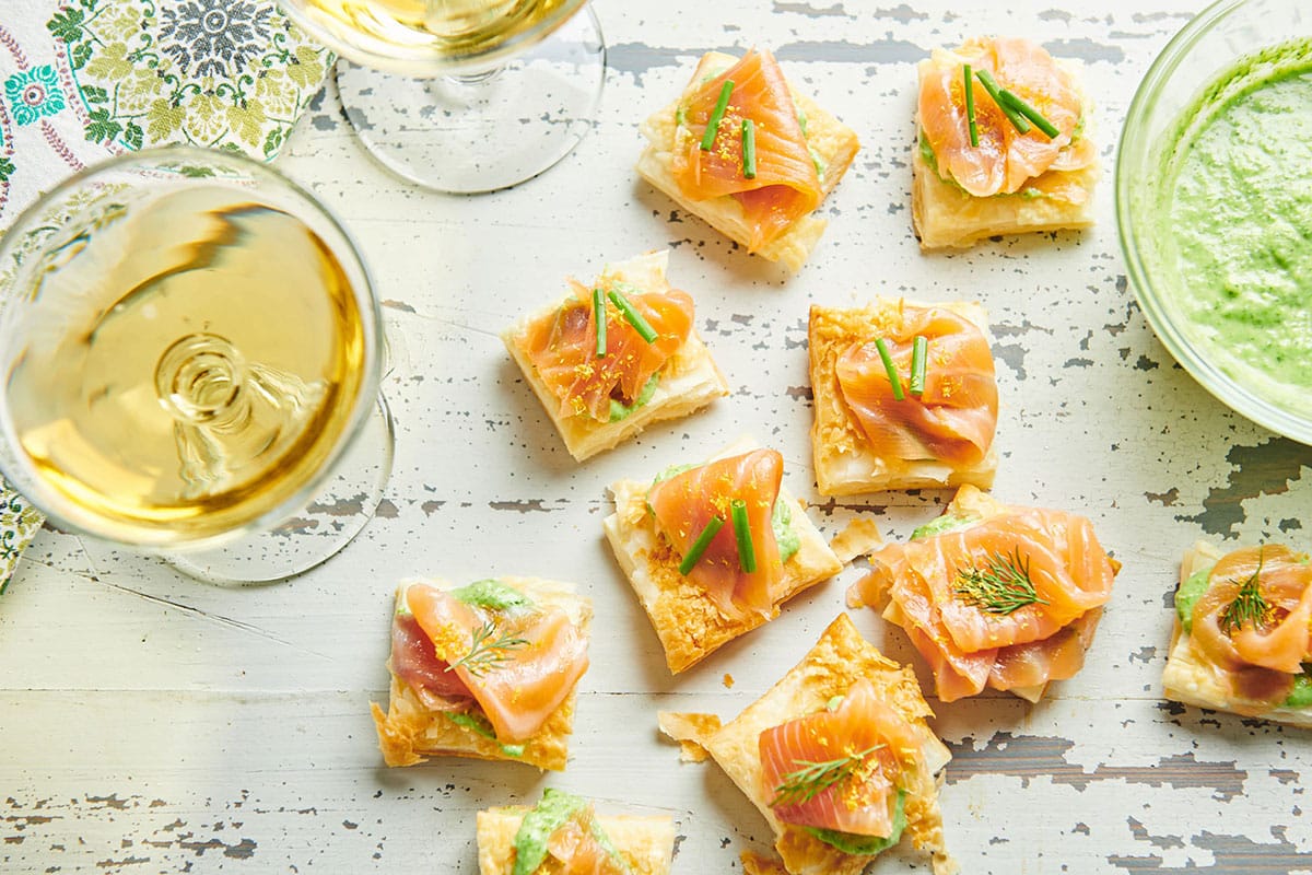 Smoked Salmon and Crème Fraiche Puff Pastry Tartlets on white wood table with wine.