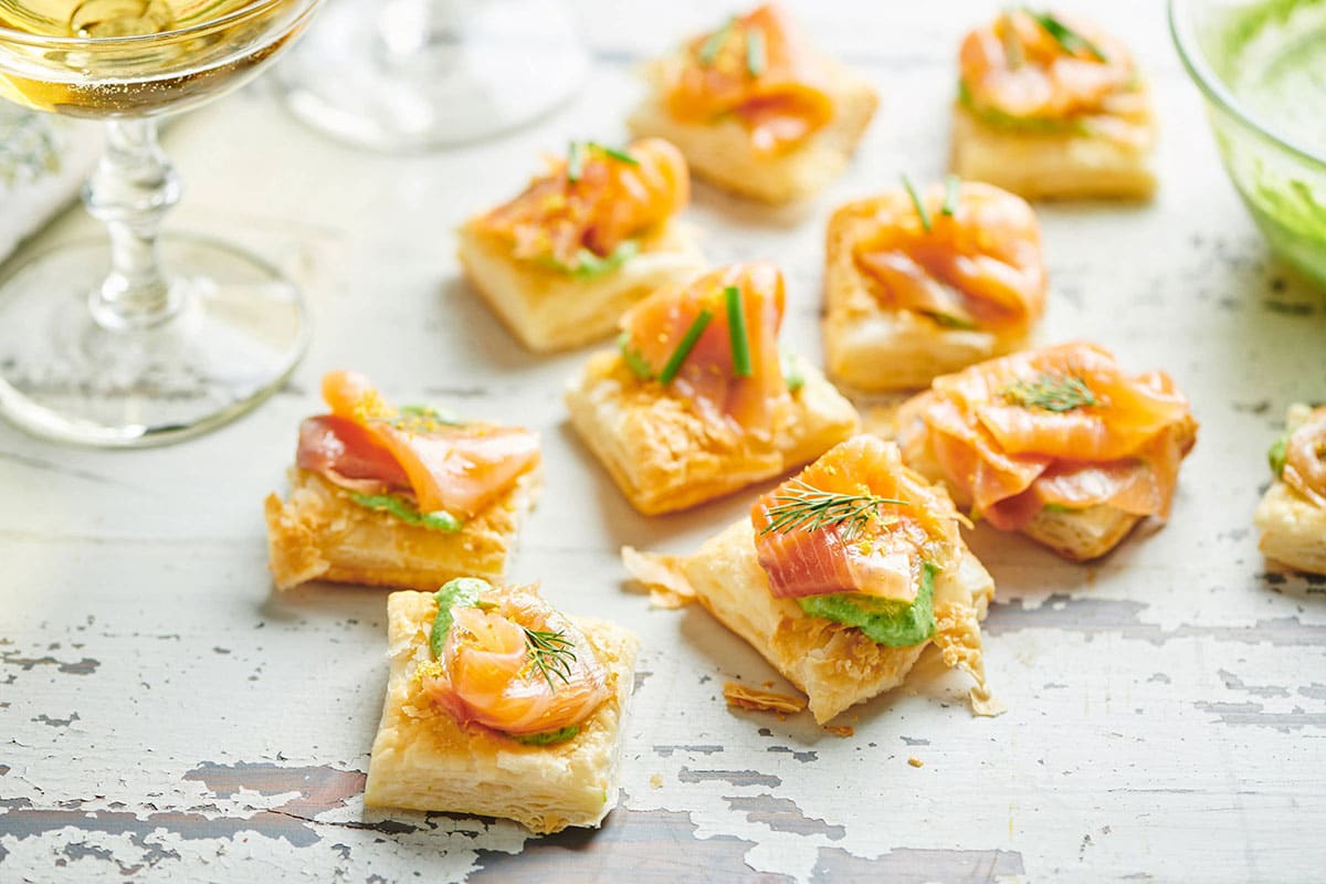 Smoked Salmon and Crème Fraiche Puff Pastry Tartlets on white wood table with glass of wine.
