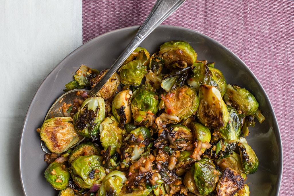 Spicy Roasted Brussels Sprouts with Kimchi Dressing on a purple and white cloth.
