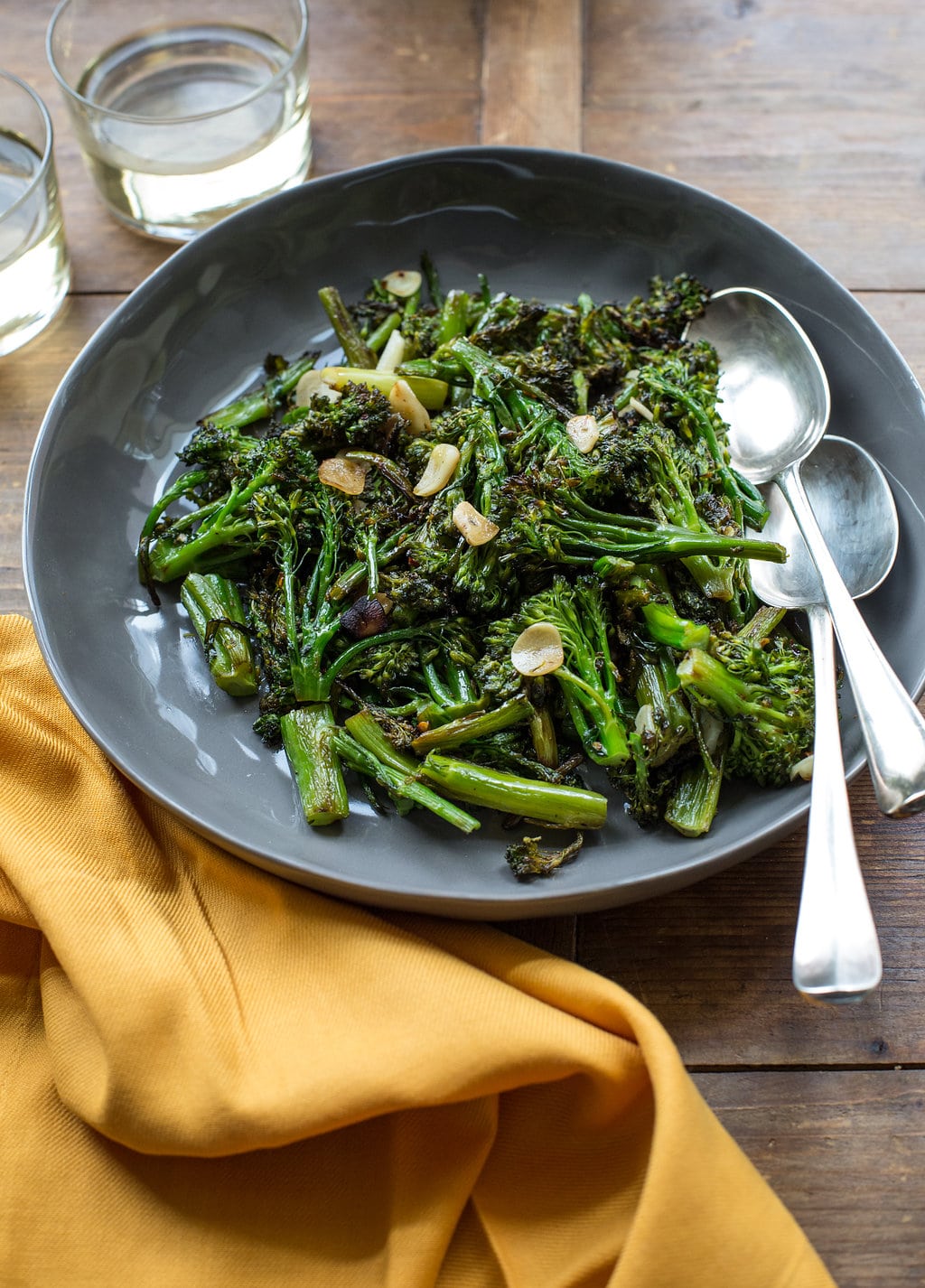 Broccolini Strascinati on grey plate with spoons and yellow napkins.