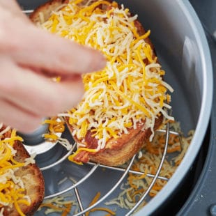 Person sprinkling shredded cheese onto bread in an Air Fryer basket.