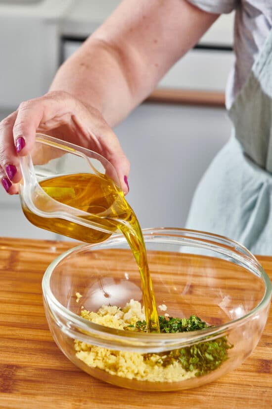 Olive oil pouring into a bowl of garlic, ginger, mint, and lime juice.