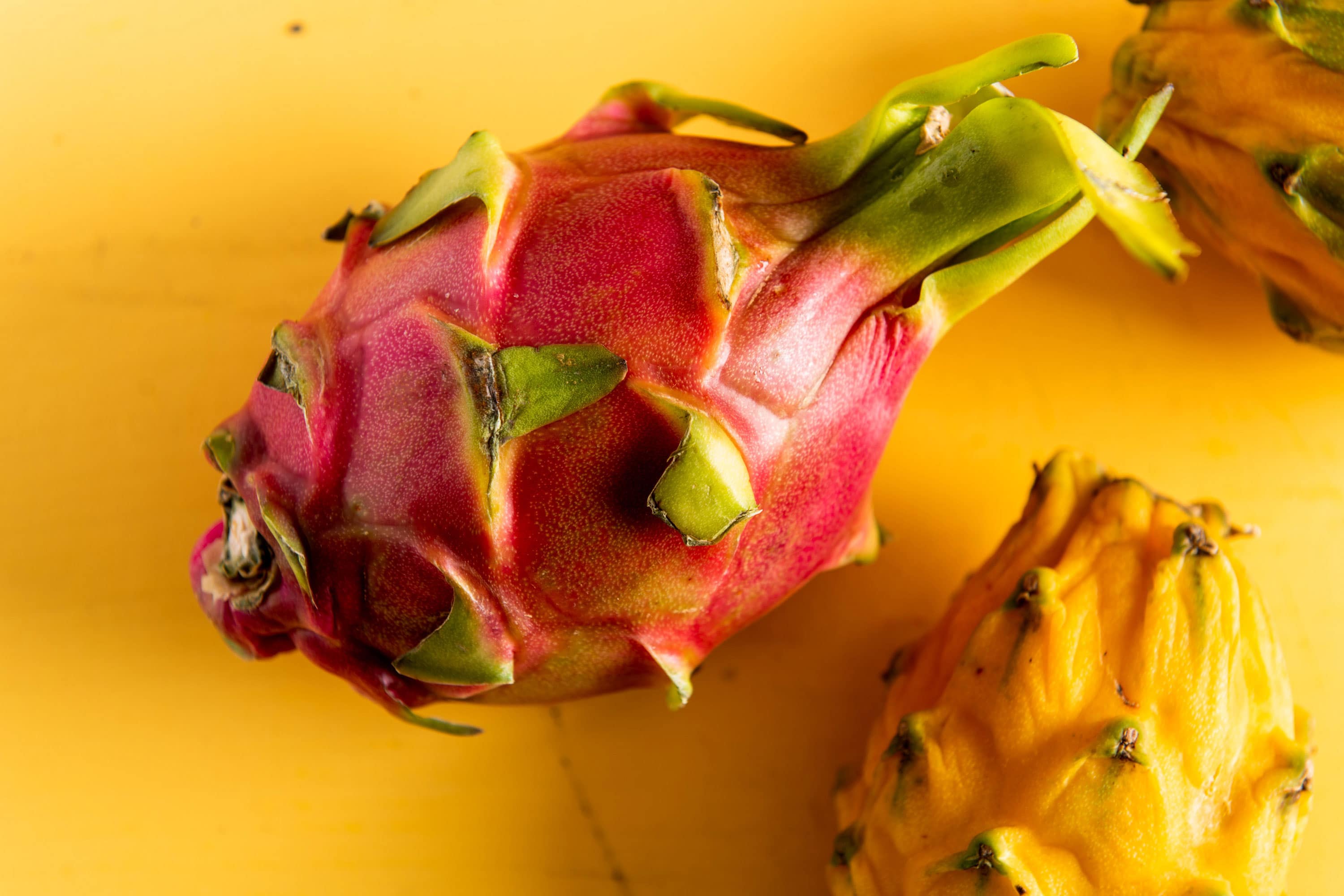 Pink uncut dragonfruit on yellow surface with yellow dragon fruit nearby.
