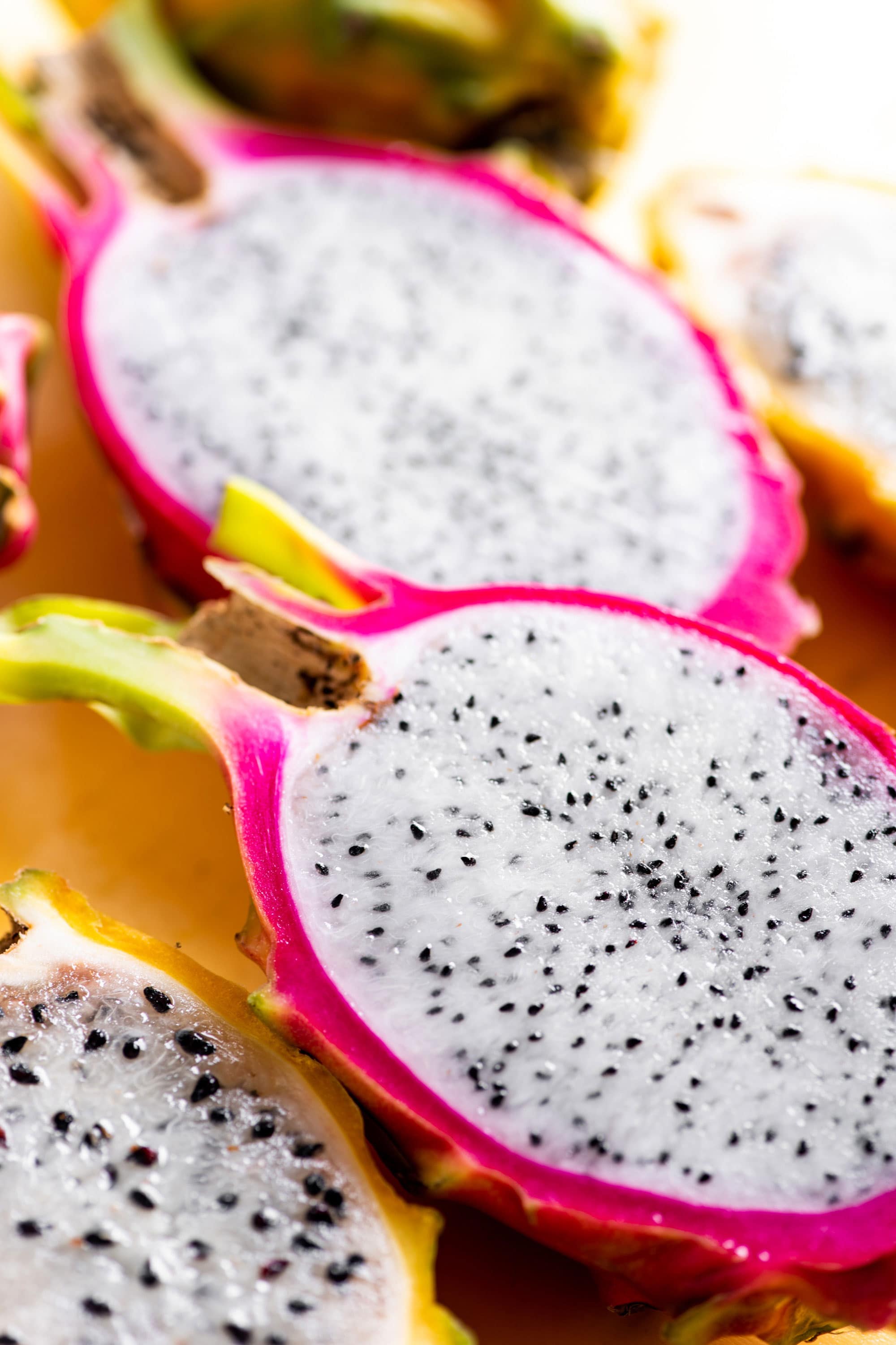 Pink dragon fruit sliced in half to show white interior with black seeds with yellow sliced dragon fruit nearby.