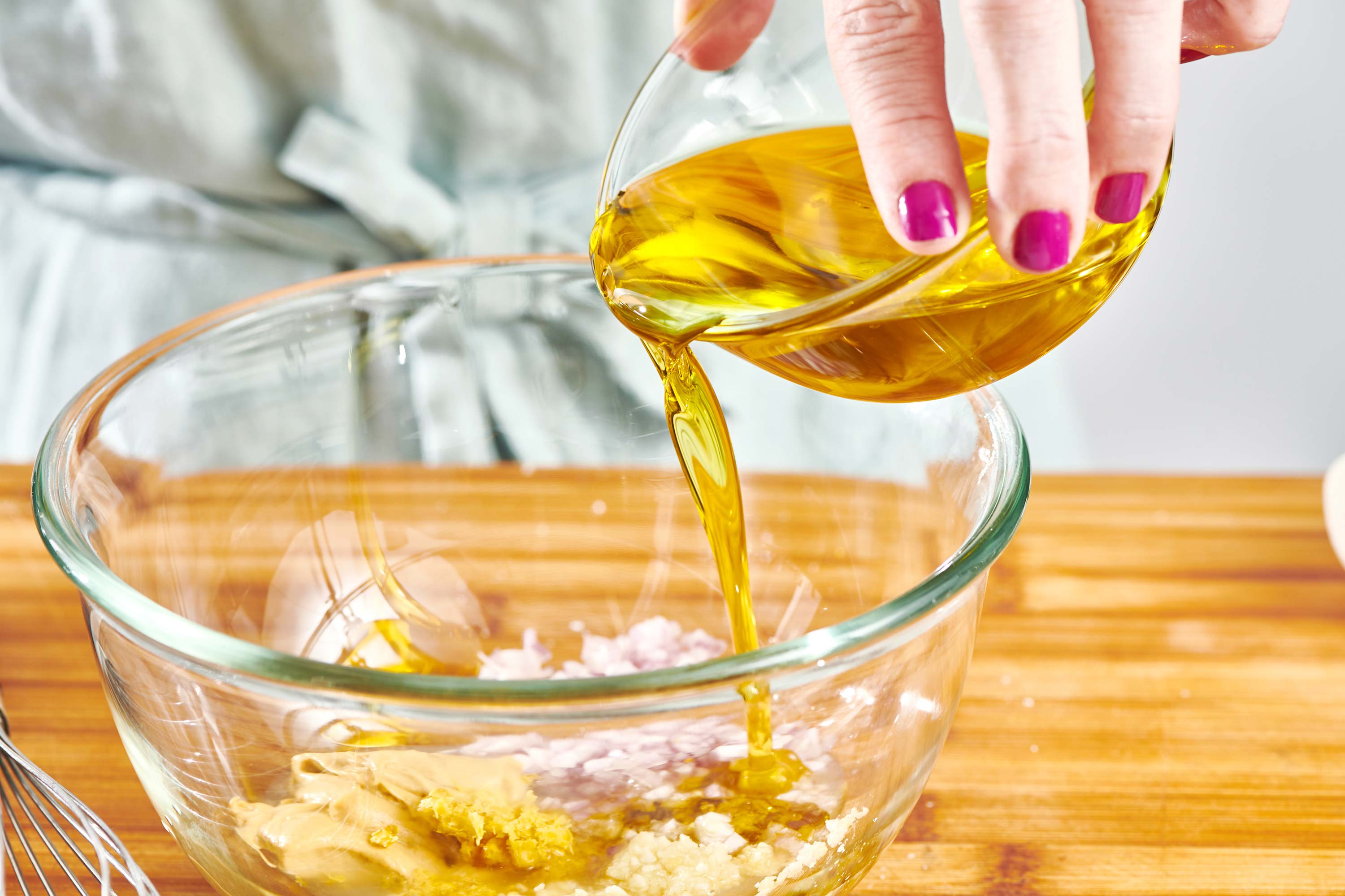 Woman pouring olive oil into bowl of Lemon Garlic Chicken Marinade.