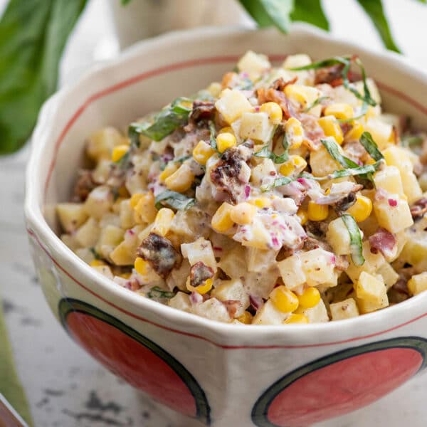Potato salad with corn and bacon in red and white bowl on table.