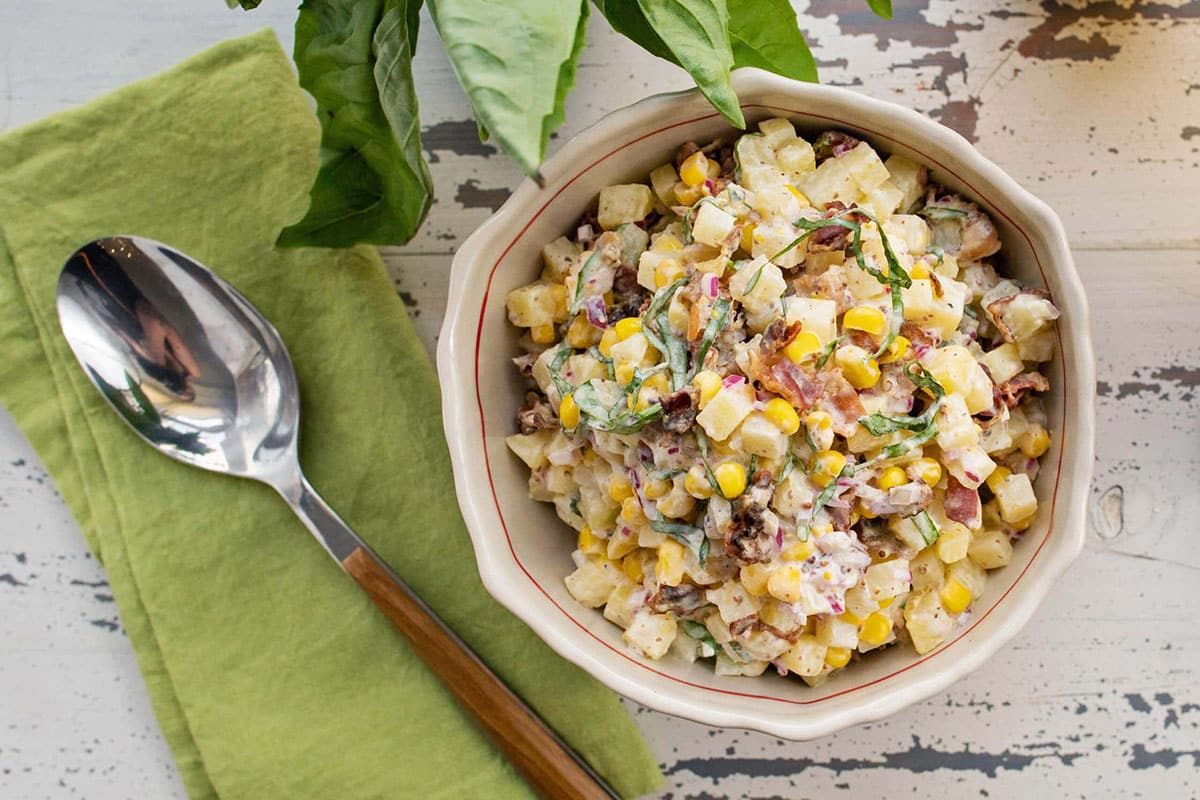 Creamy Corn and Potato Salad in bowl on table with napkin and spoon.