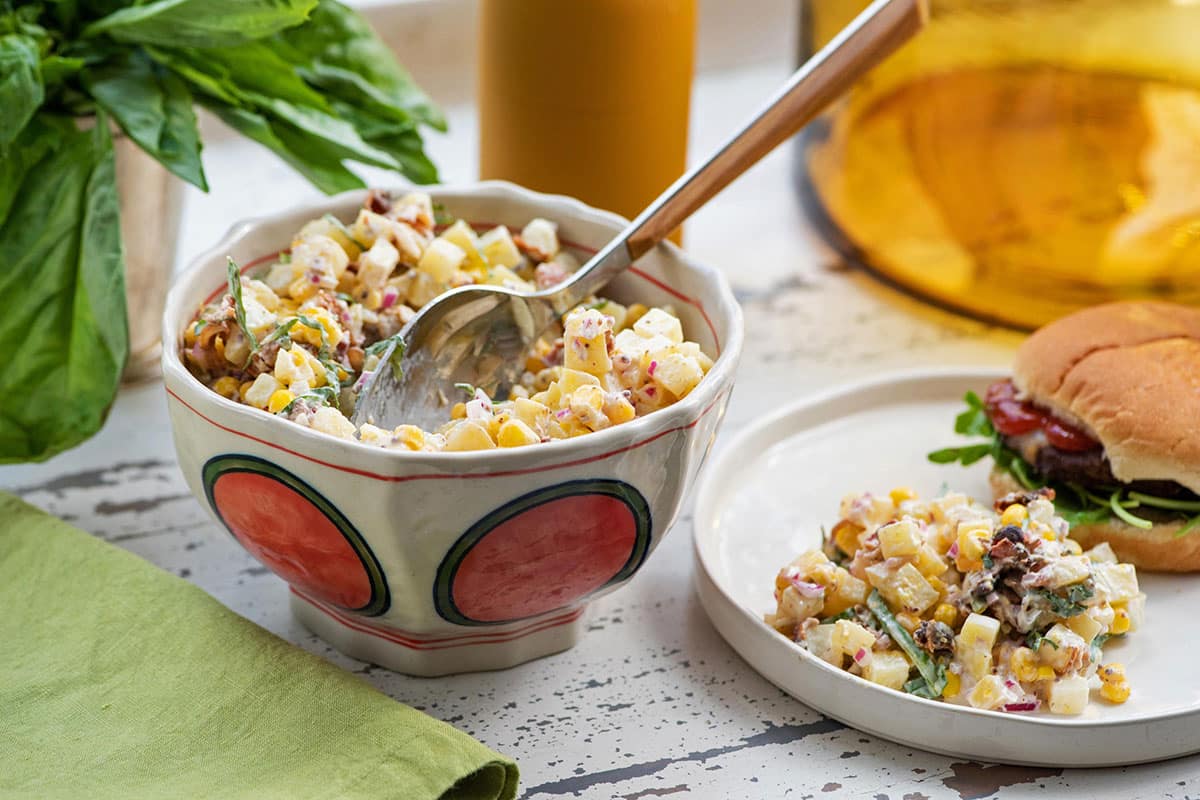 Creamy potato, corn, and bacon salad in bowl and on plate.
