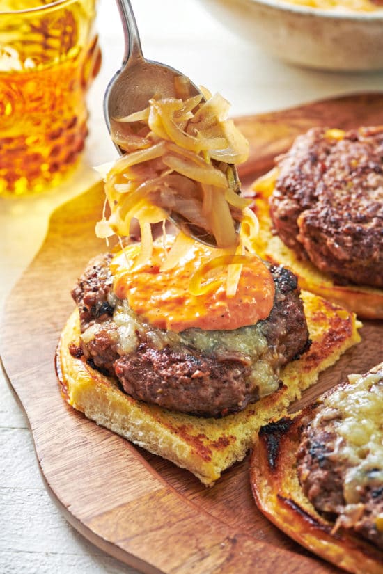 Spoon scooping caramelized onions onto a Lamb Burger.