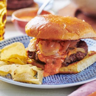 Spanish Lamb Burger with Romesco Sauce and Caramelized Onions on a plate with chips.