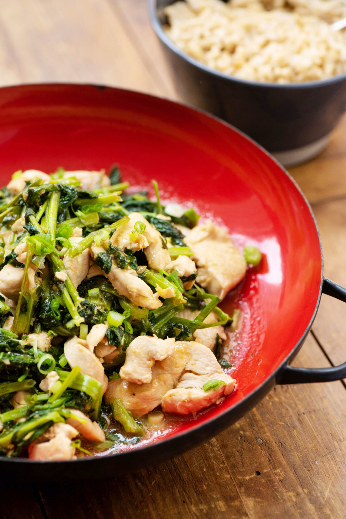 Stir fried chicken with pea shoots in a red bowl.
