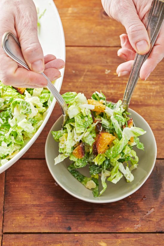 Woman scooping Caesar Salad with Garlicky Croutons into a small bowl.