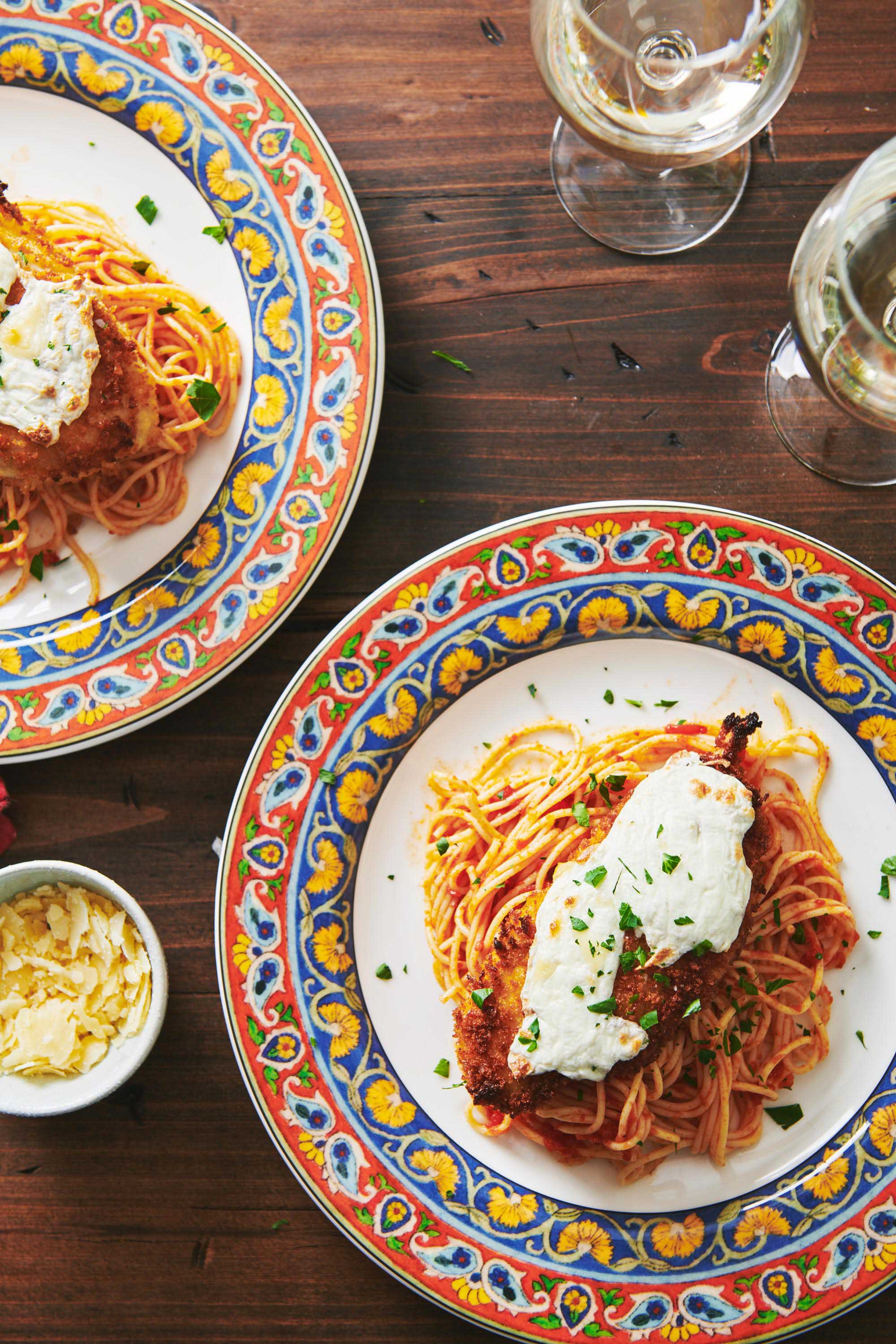 Two colorful plates of Chicken Parmigiana on wood table.