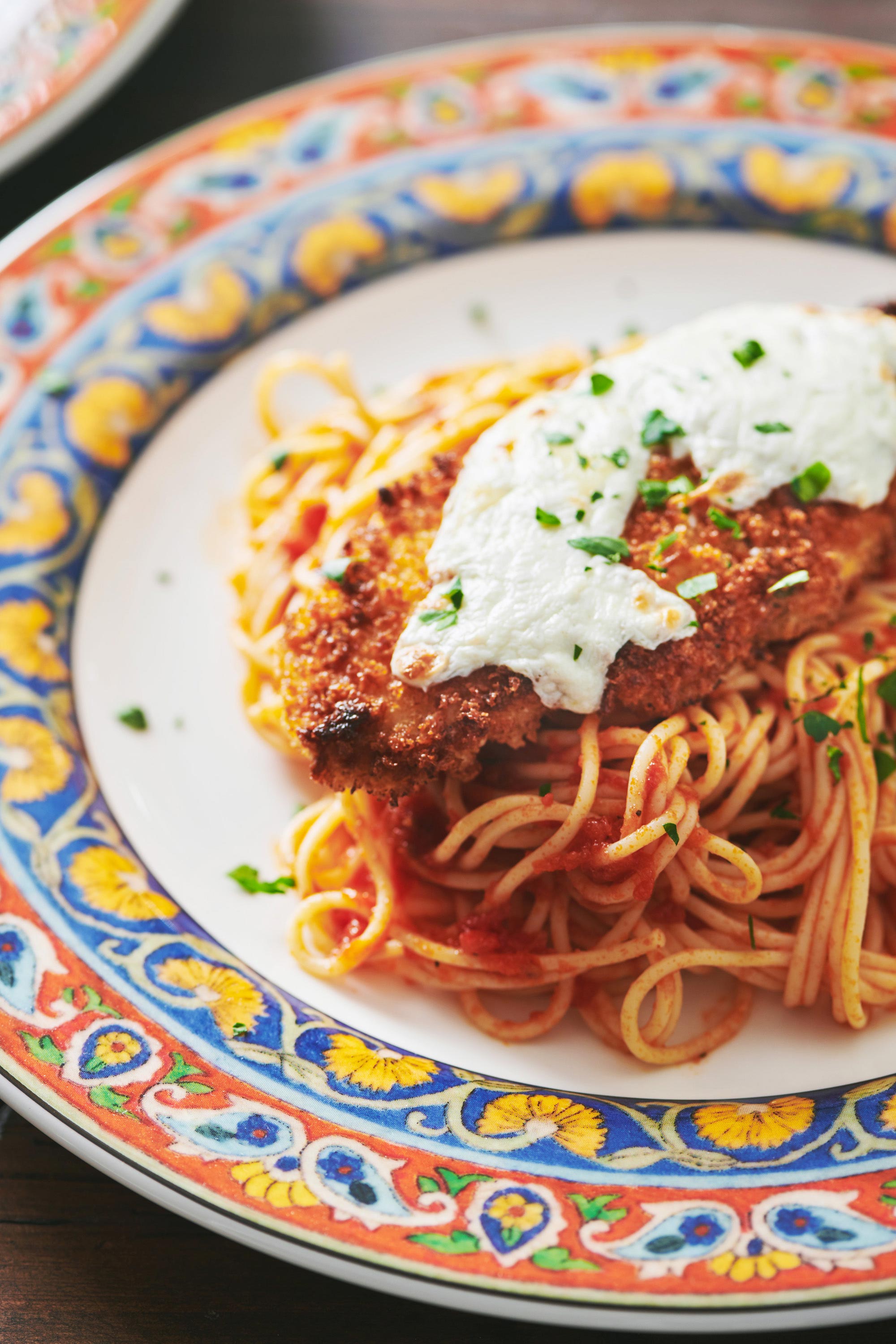 Chicken Parmigiana on a plate with a colorful rim served over spaghetti