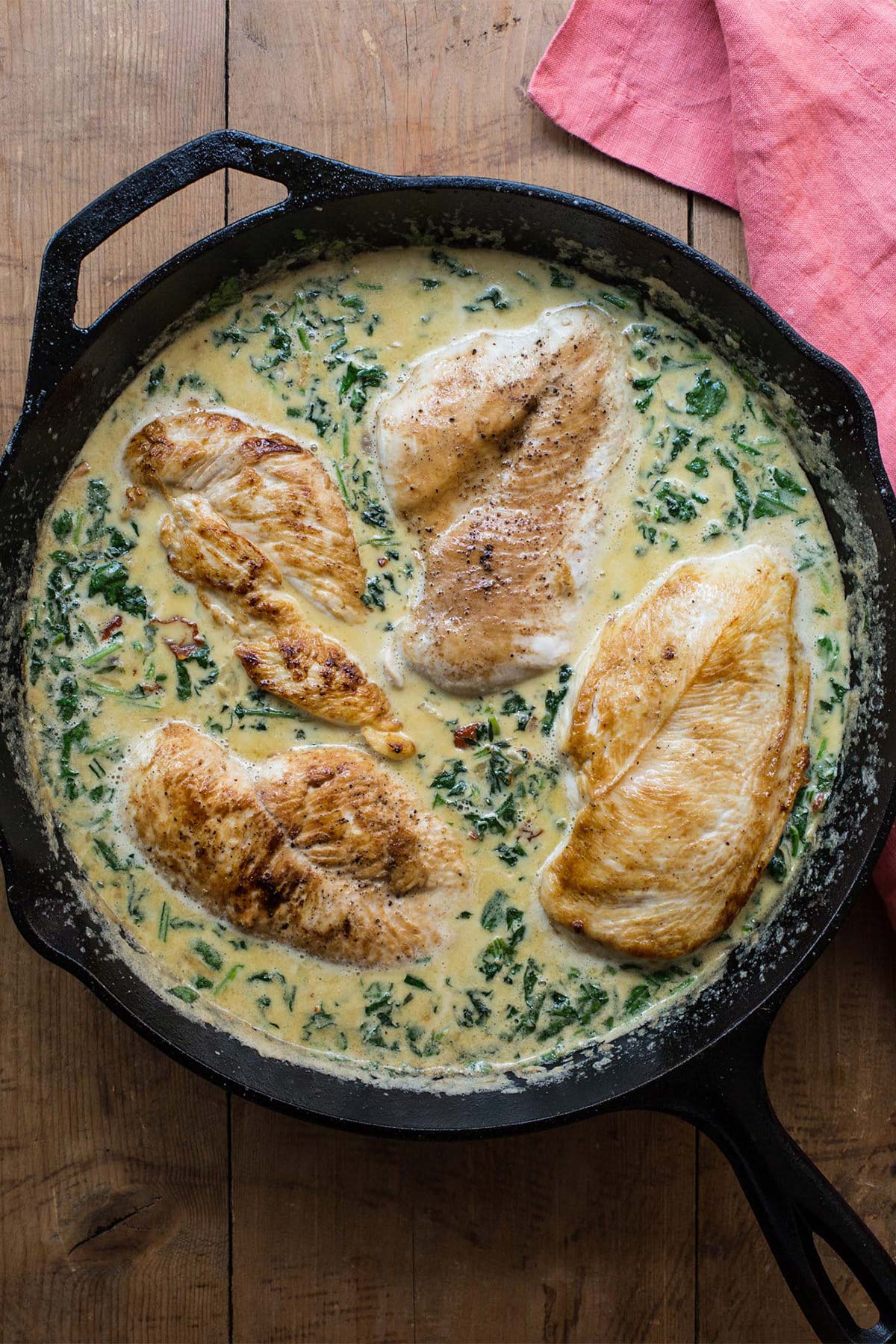 Cast iron skillet with chicken in creamy spinach and sun-dried tomato sauce.