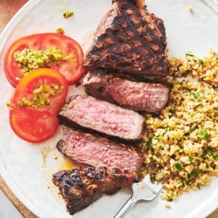 Grains, tomatoes, and Grilled Marinated NY Strip Steak on a plate.