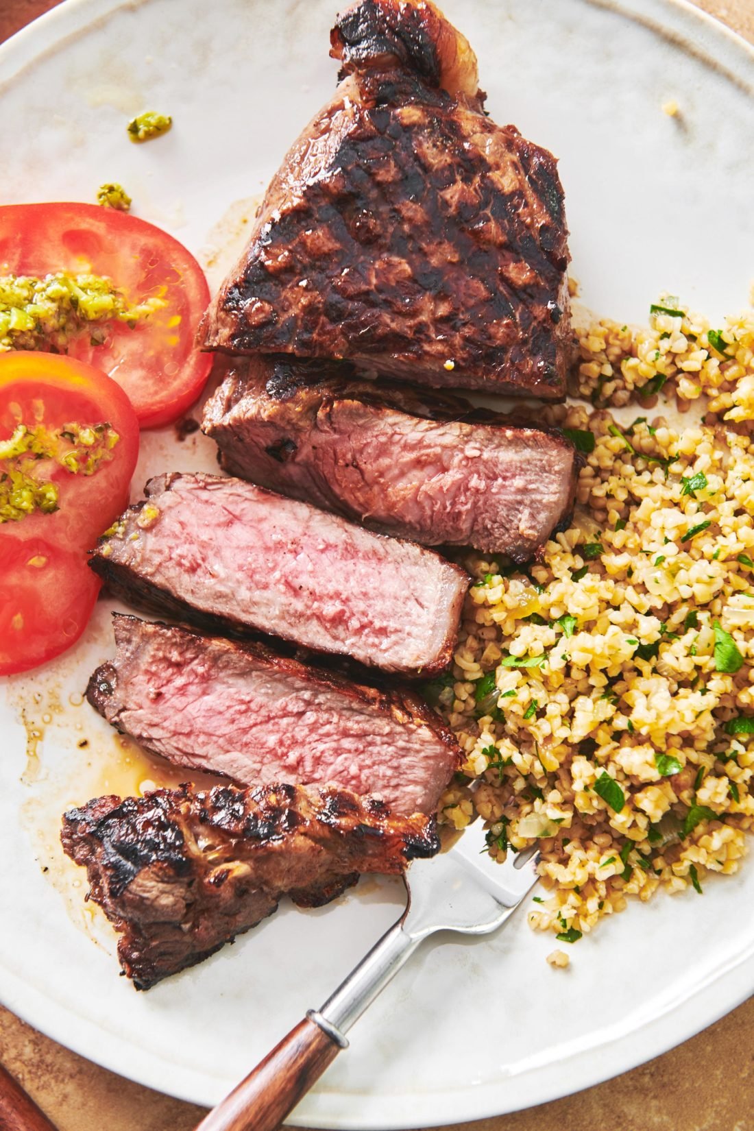 Plate with Grilled Marinated NY Strip Steak, grains, and tomatoes.