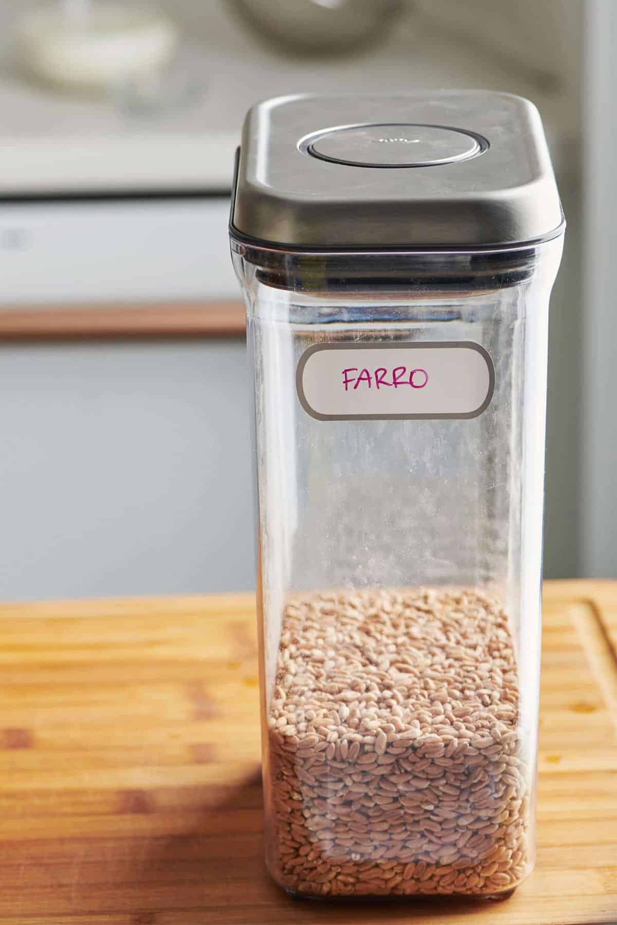 Uncooked farro in tall container on kitchen counter.