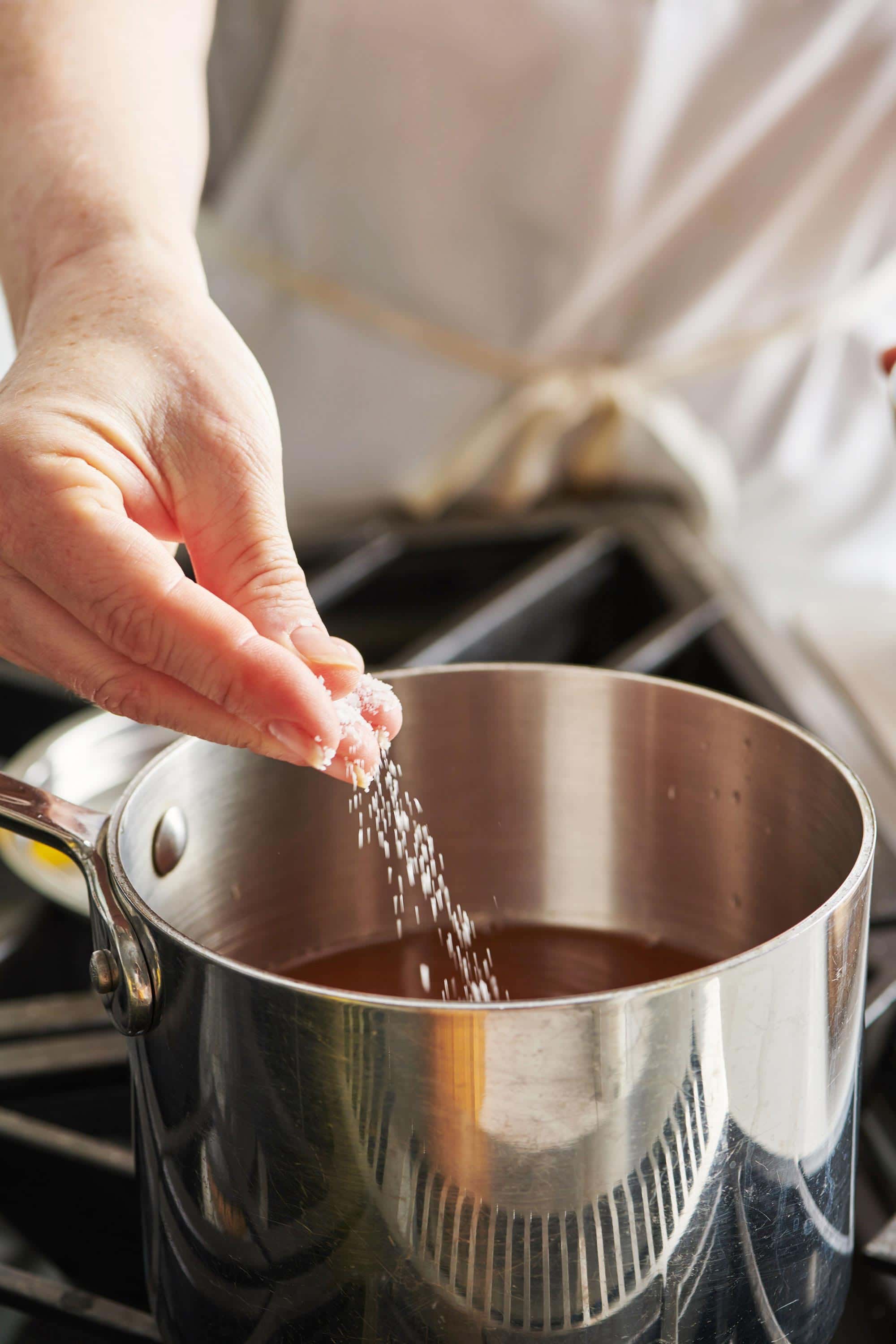 Woman adding salt to pot with broth in it.