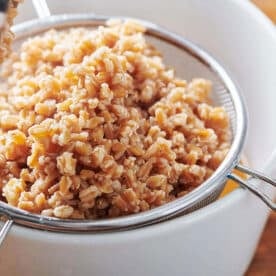 Cooked farro in metal strainer draining over bowl.