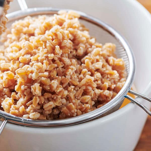 Cooked farro in metal strainer draining over bowl.