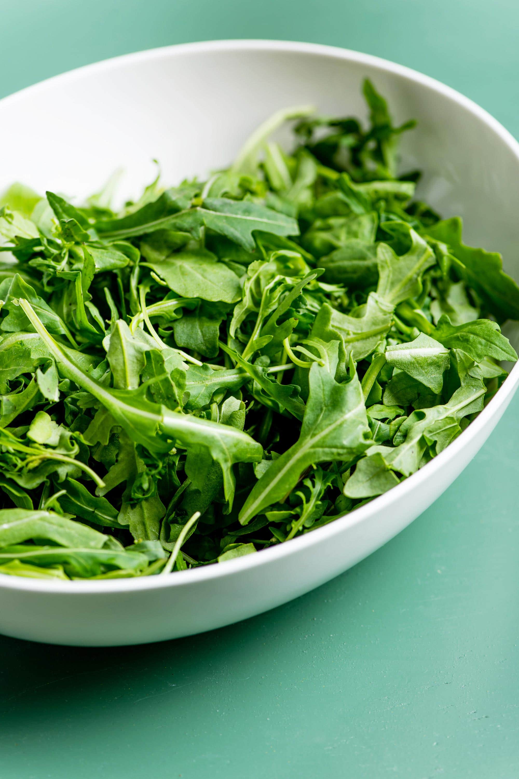 Fresh arugula in white bowl.