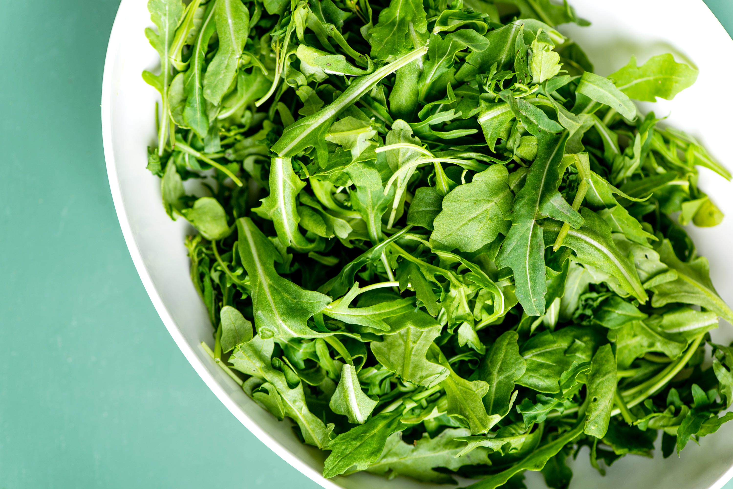 White bowl full of fresh arugula leaves.