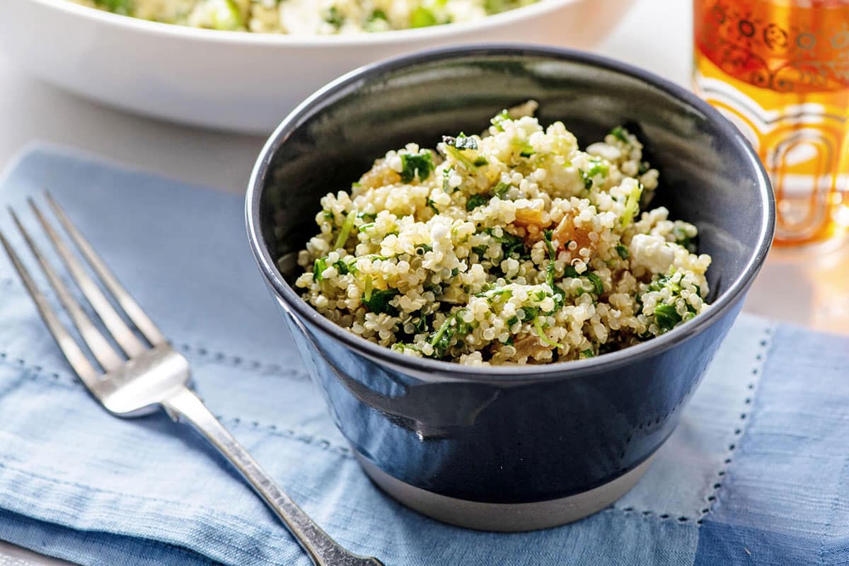 Blue bowl on table filled with kale and quinoa salad.