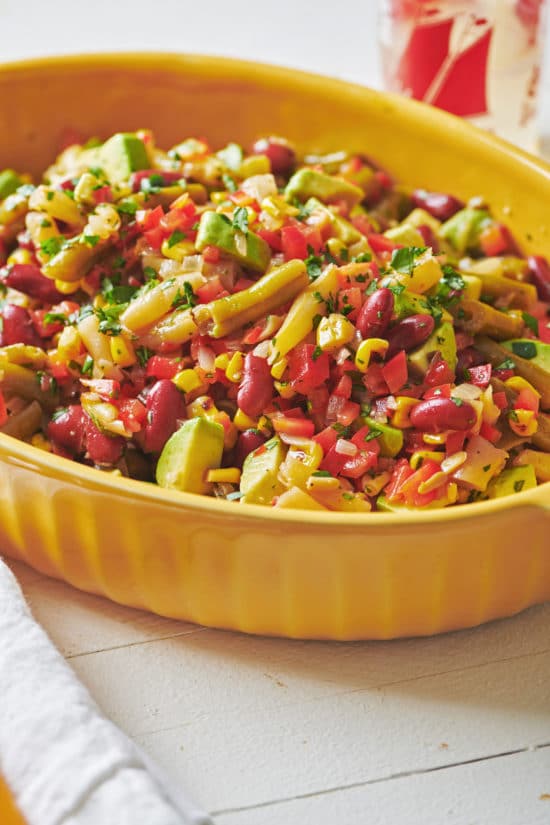 Colorful Mexican Avocado, Corn and Three Bean Salad in a yellow dish.