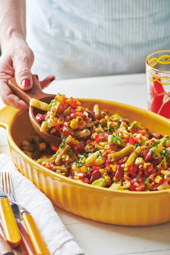 Woman scooping Mexican Avocado, Corn and Three Bean Salad with a wooden spoon.