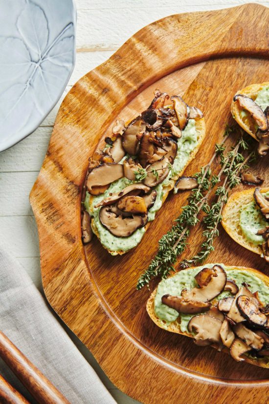 Mushroom Bruschetta with Herbed Mayonnaise next to sprigs of thyme on a wooden plate.