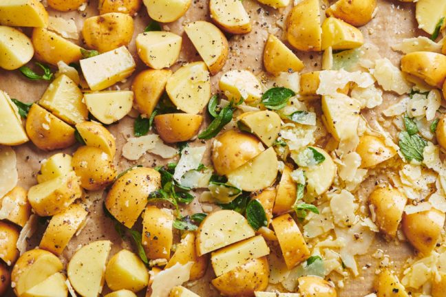 Diced potatoes on a baking sheet with parmesan cheese and seasonings.