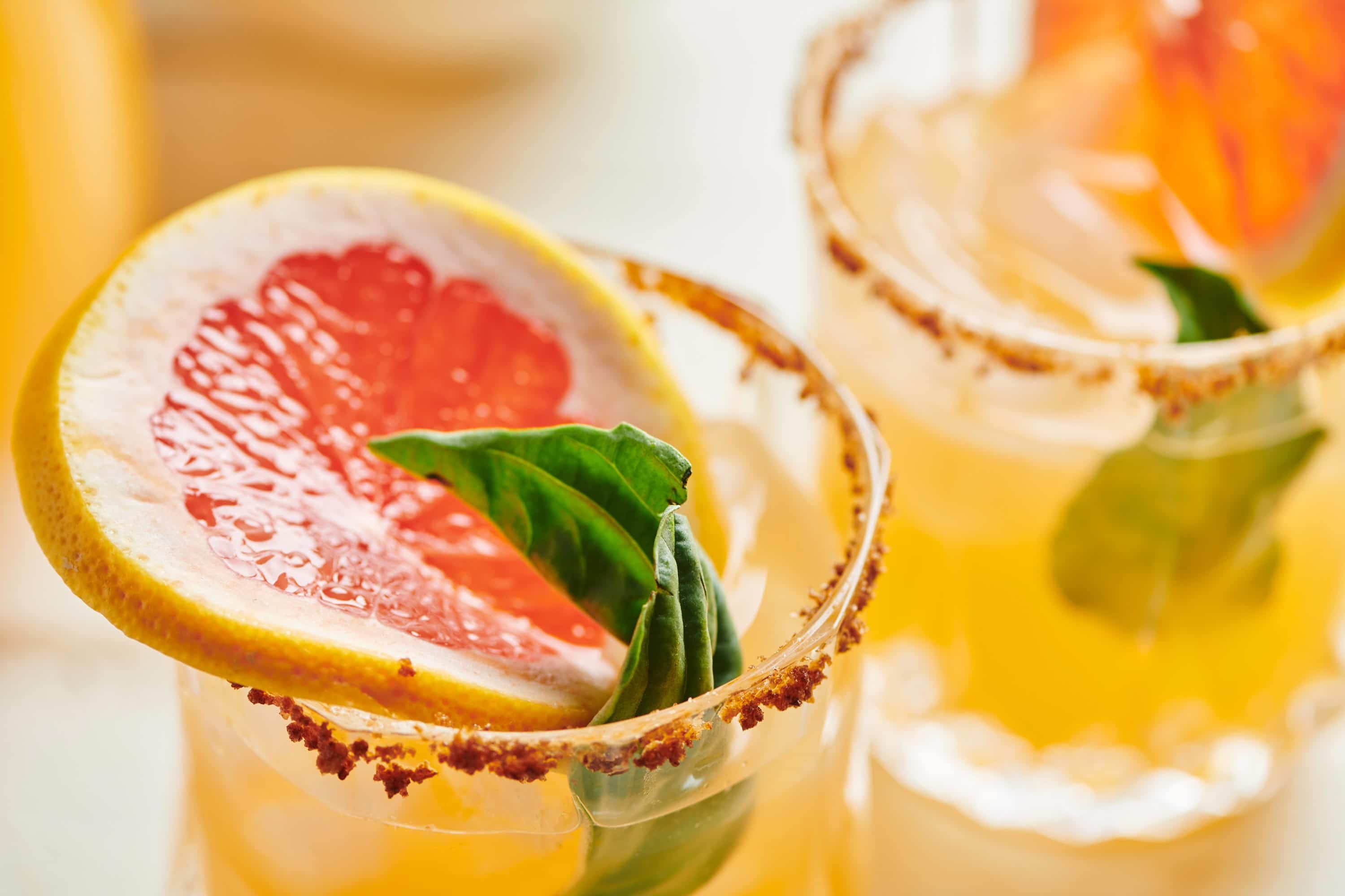 Slice of grapefruit in a glass of Pomelo Paloma rimmed with sriracha salt.