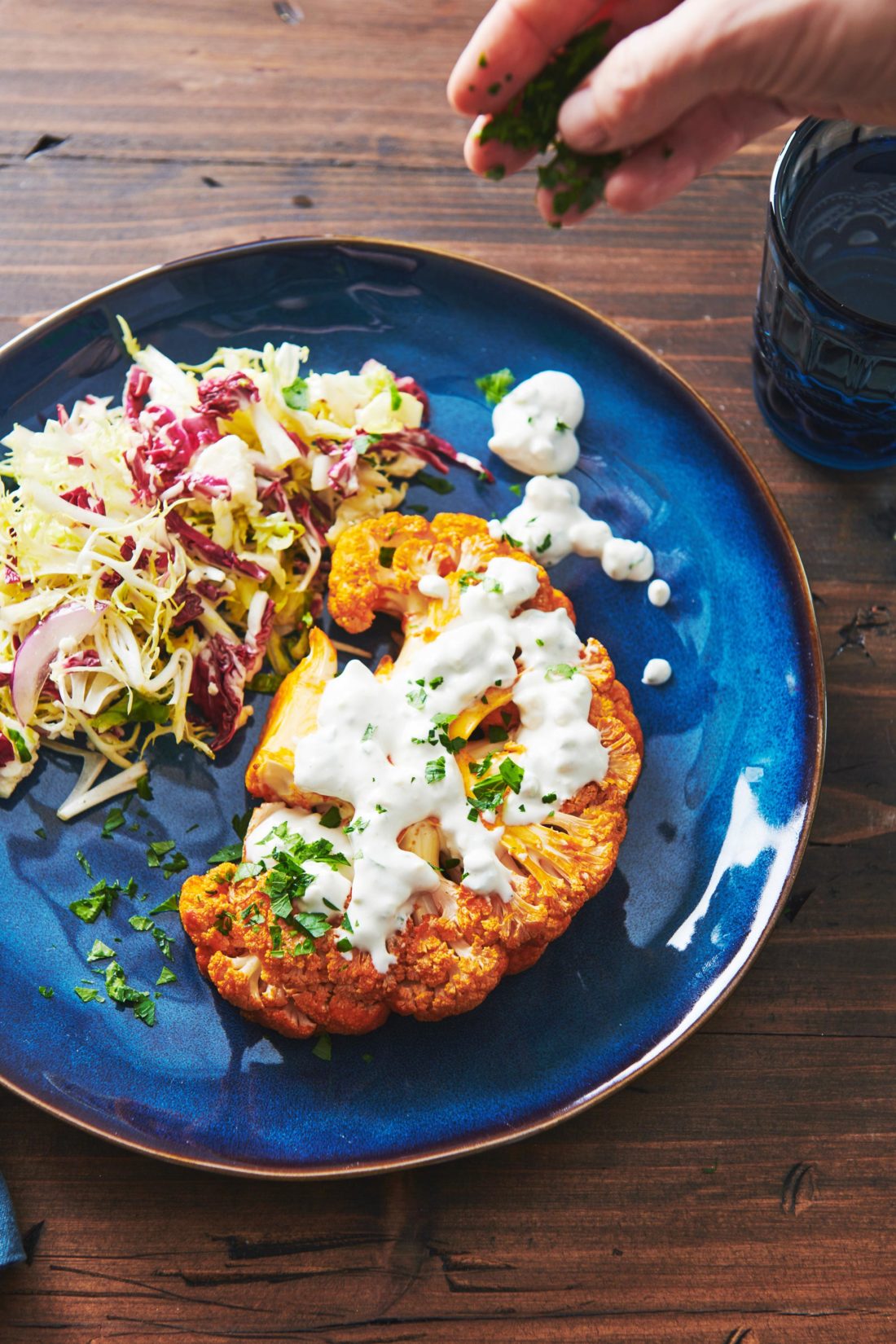 Roasted Buffalo Cauliflower Steak topped with Bleu Cheese dip on a plate with salad.