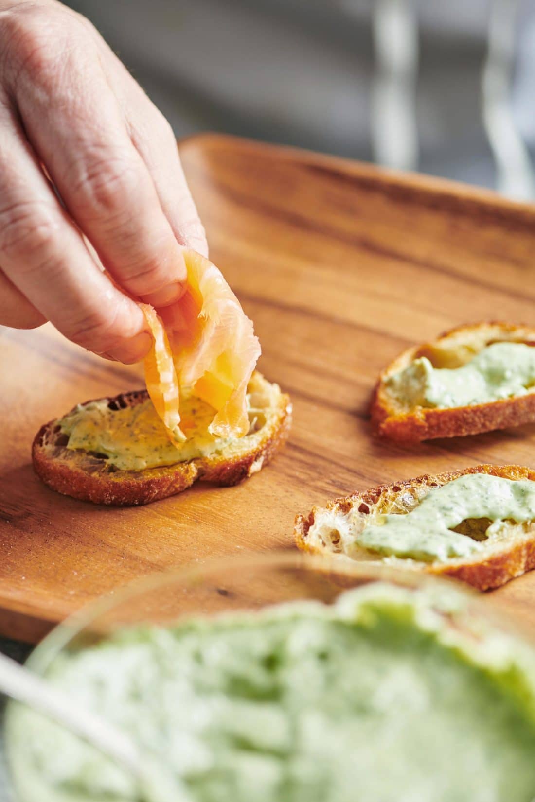 Woman placing Smoked Salmon onto a Crostini with Herbed Mayonnaise.