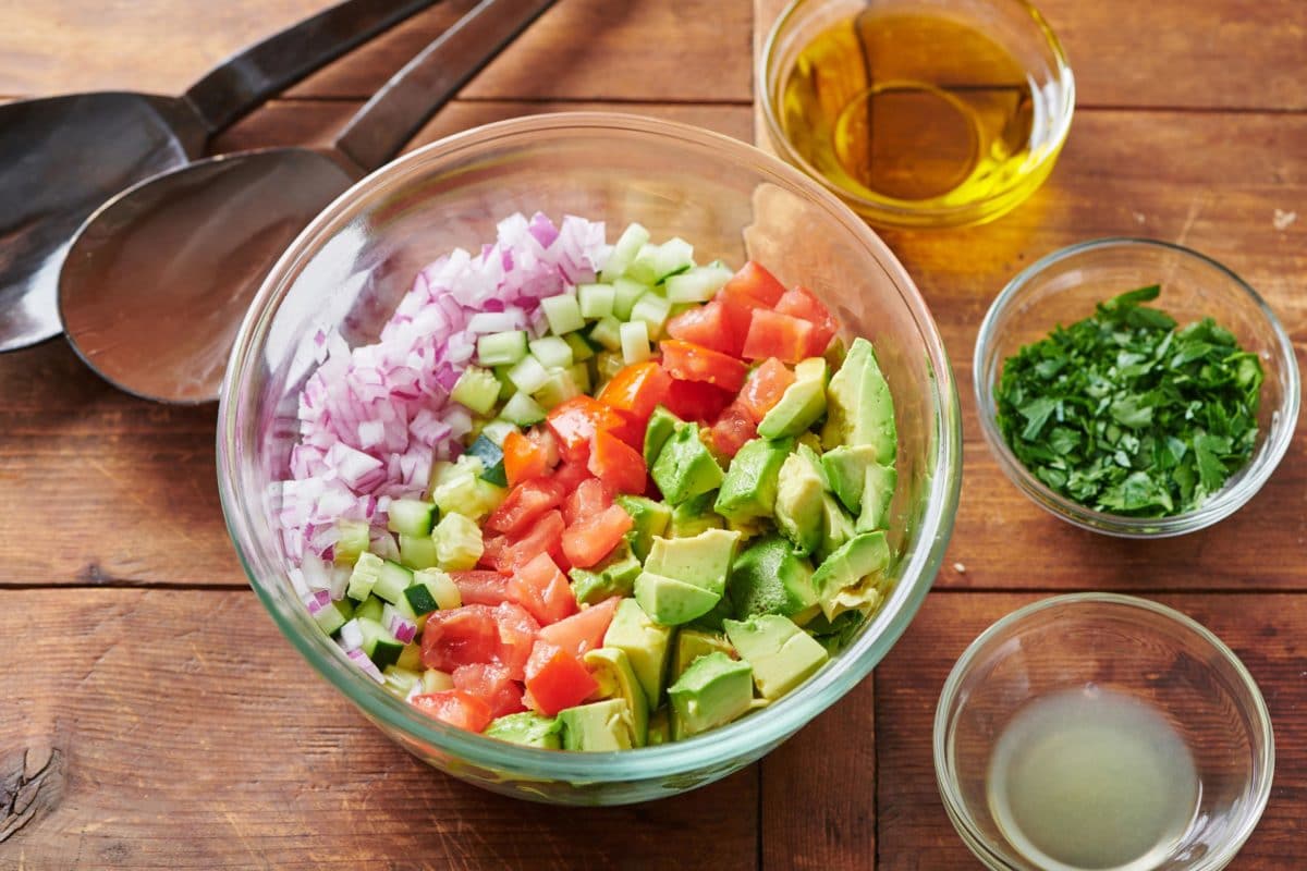 Diced Tomatos, Avocados, red onion, and Cucumber in a glass bowl.