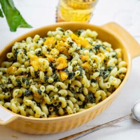 Cavatappi with Roasted Cherry Tomatoes and Pesto in yellow serving dish on table.