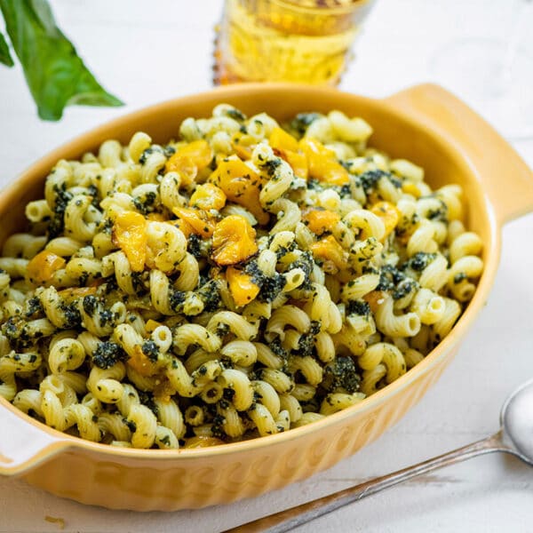 Cavatappi with Roasted Cherry Tomatoes and Pesto in yellow serving dish on table.