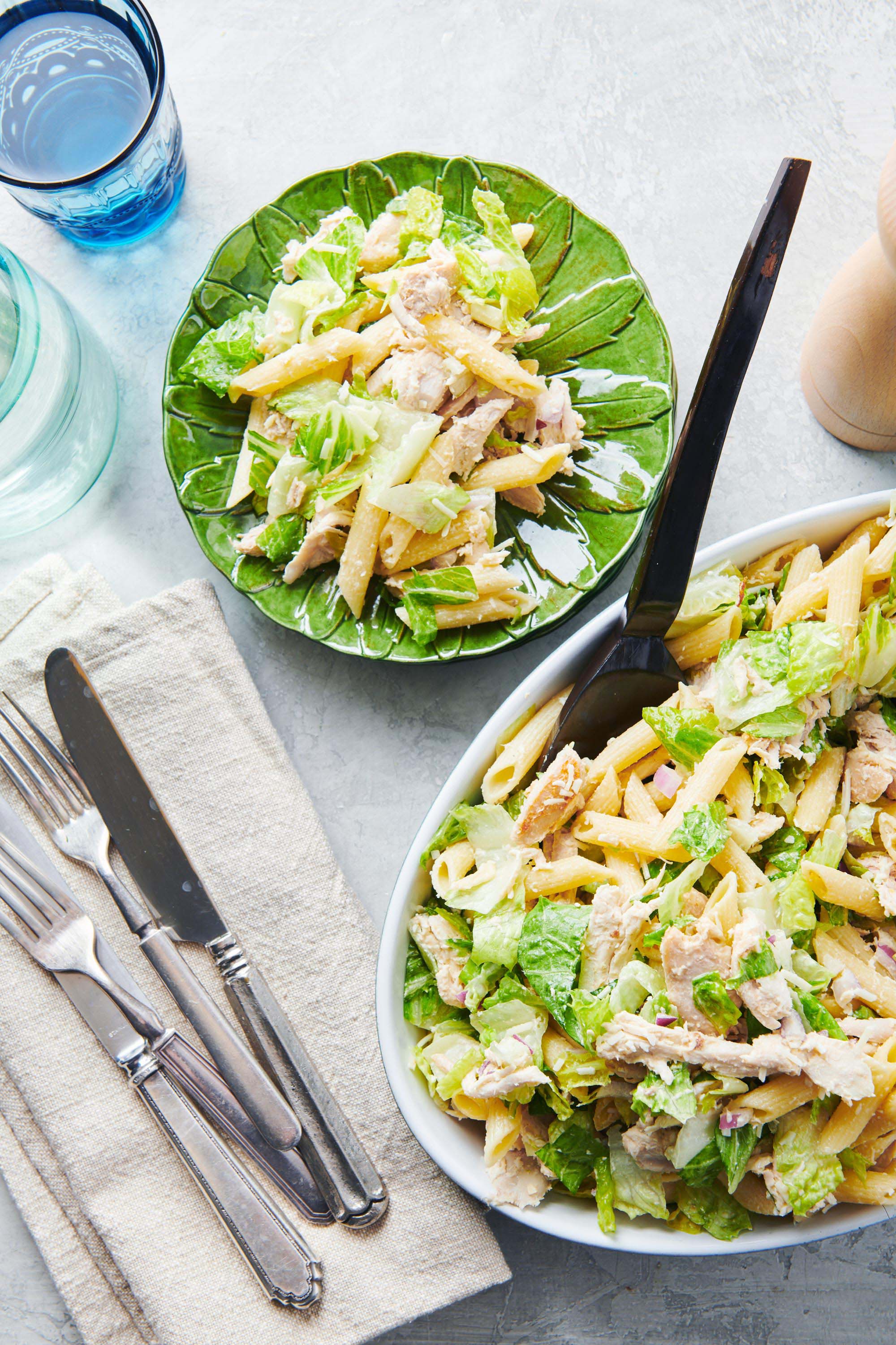 Chicken Caesar Pasta Salad in a serving bowl with forks and knives on a napkin.