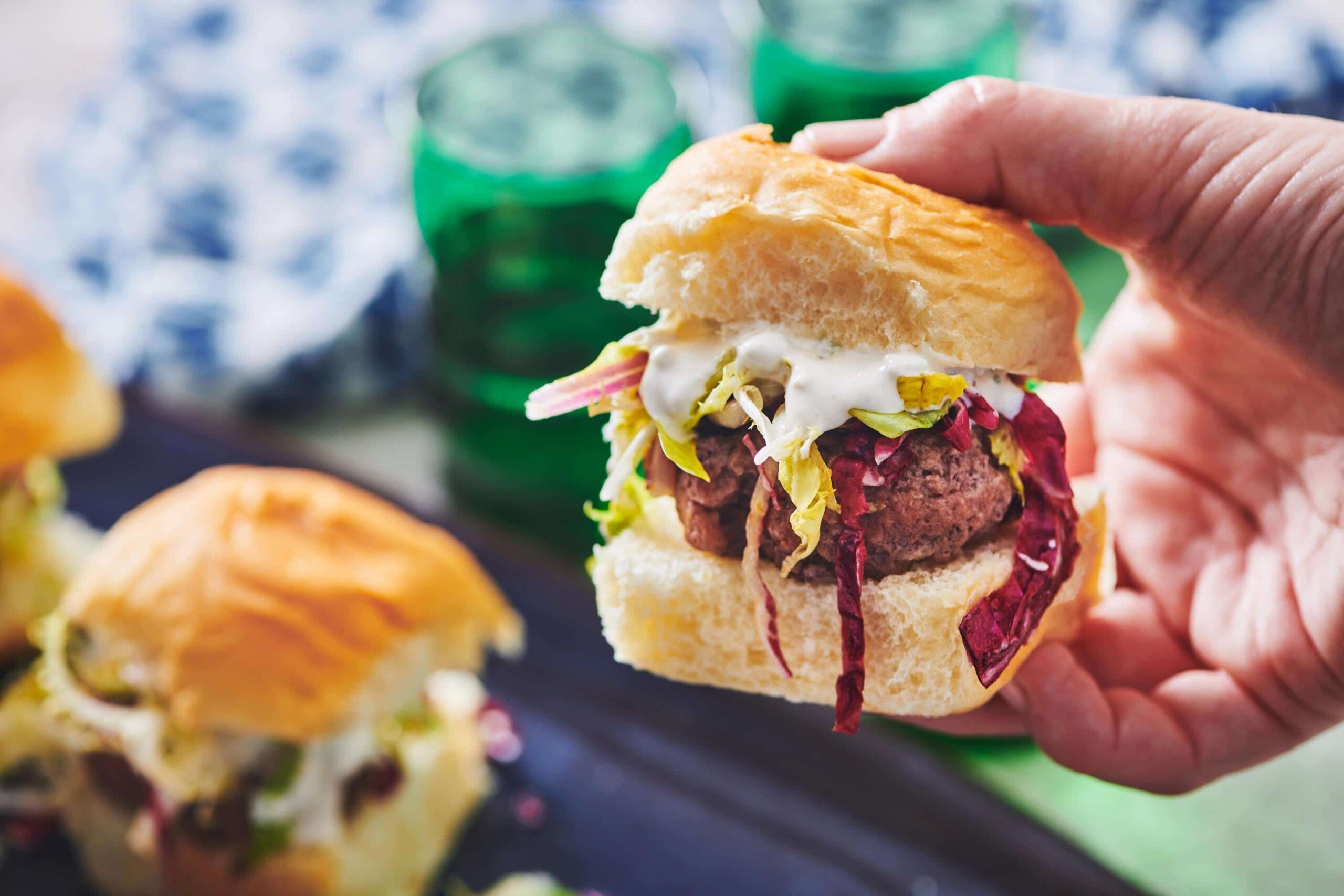 Person holding Chipotle Slider with slaw and blue cheese over table.