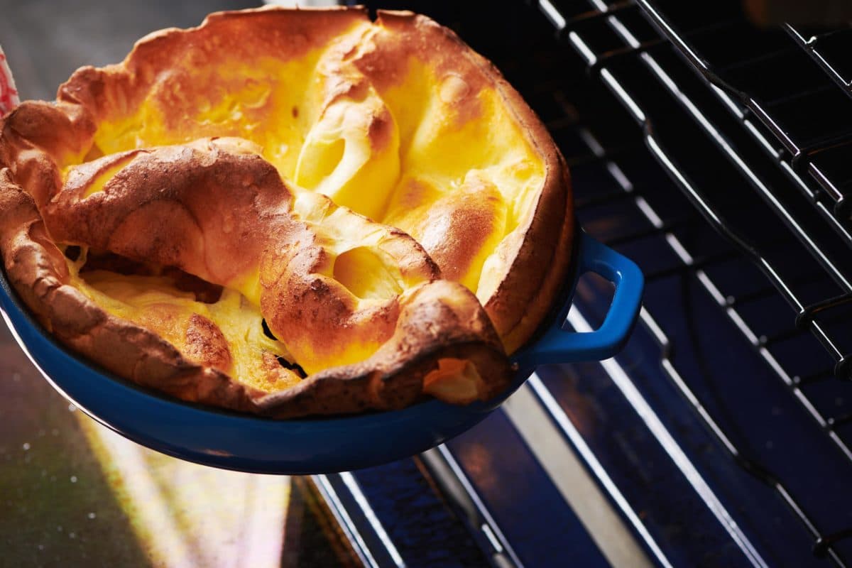 Blue pan of Dutch Baby Pancake with Sauteed Apples being pulled from an oven.