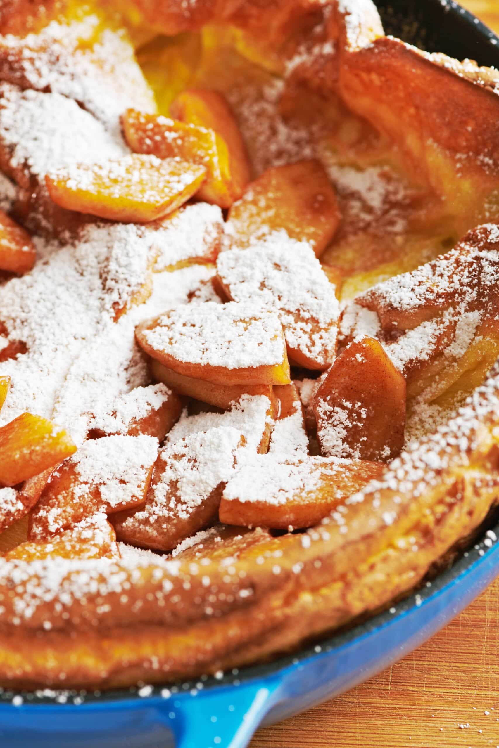 Dutch Baby Pancake with Sauteed Apples with powdered sugar in blue pan.