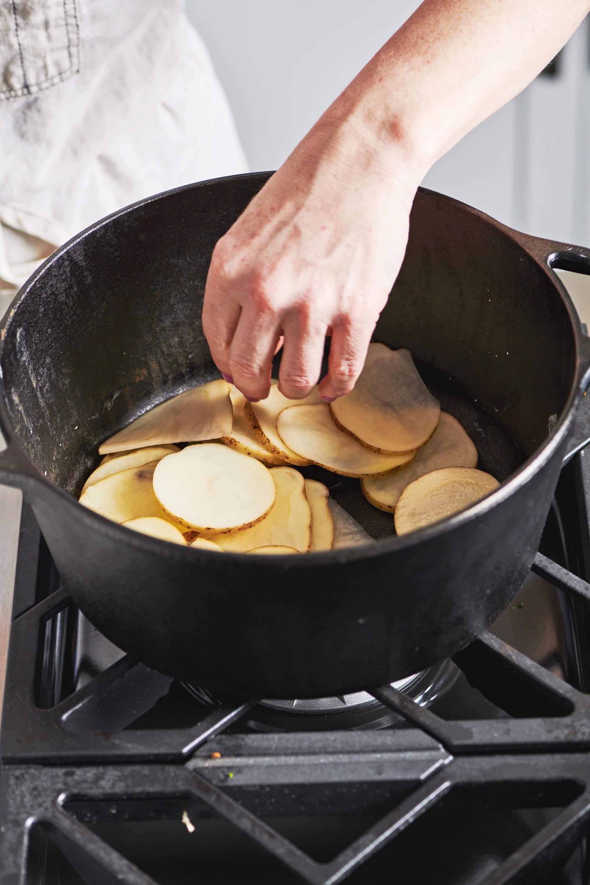 Woman placing potatoes in a cast iron pot.