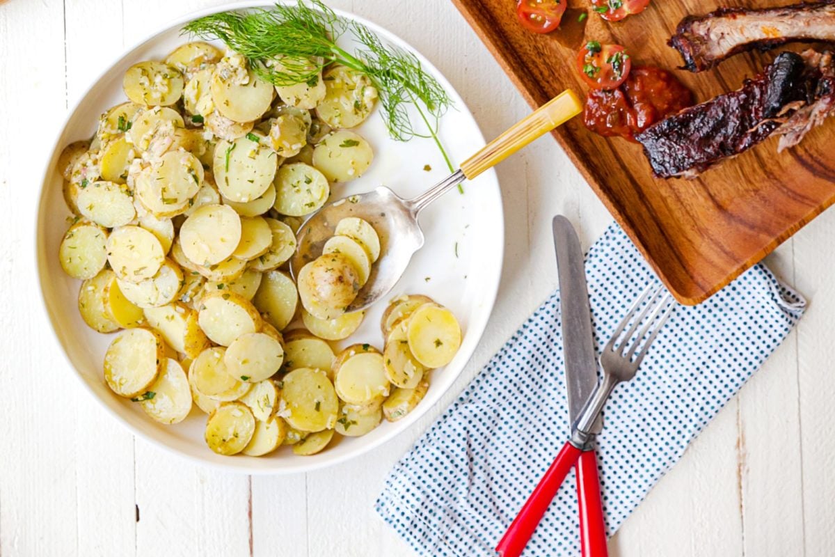 Bowl with French Potato Salad set on a table with utensils and other foods.