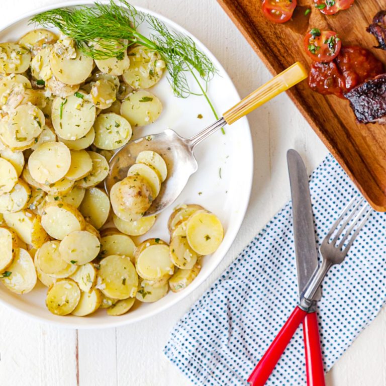 Bowl with French Potato Salad set on a table with utensils and other foods.
