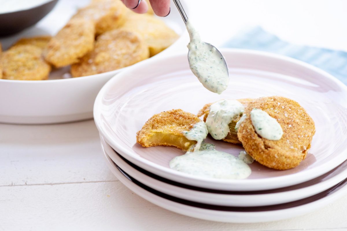 Spoon drizzling Green Goddess Dressing onto Fried Green Tomatoes.