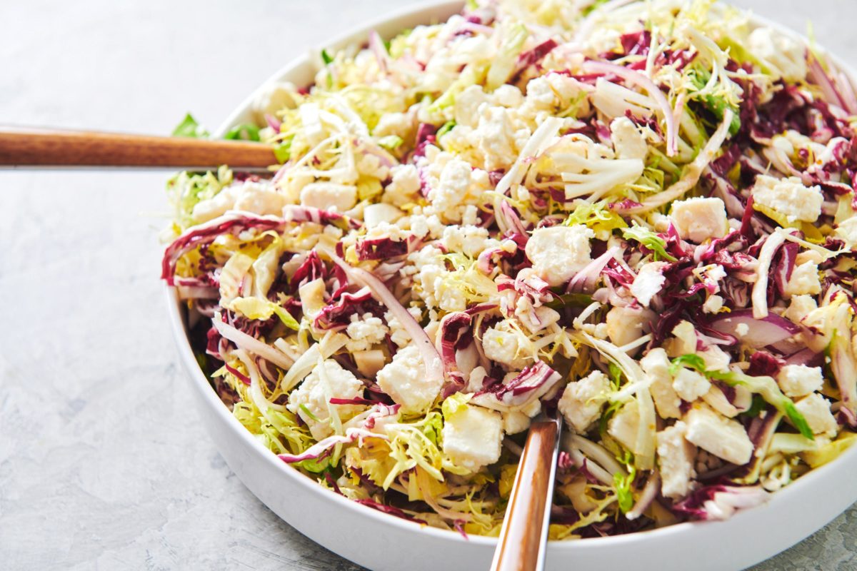 Bowl of Frisee, Radicchio and Escarole Salad with Citrus Dressing being tossed with utensils.