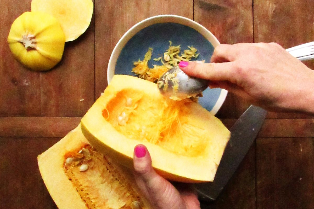 Woman scooping seeds out of a halved spaghetti squash.